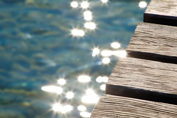 A wooden deck with a blurred background of water and sunlight reflections. - Concept Village Piccola Gardiola (San Felice del Benaco)