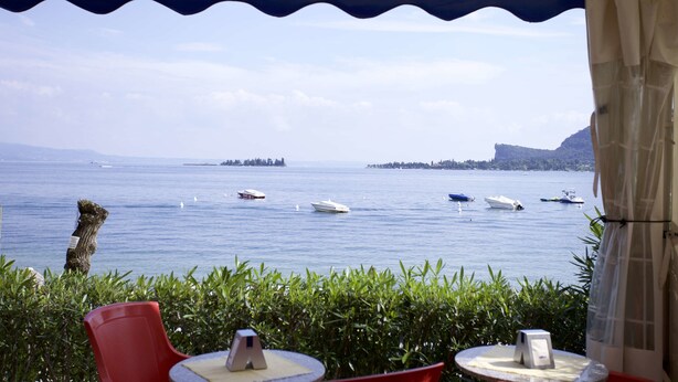 A terrace with a view of the sea, featuring several boats and a distant island. - Concept Village Piccola Gardiola (San Felice del Benaco)