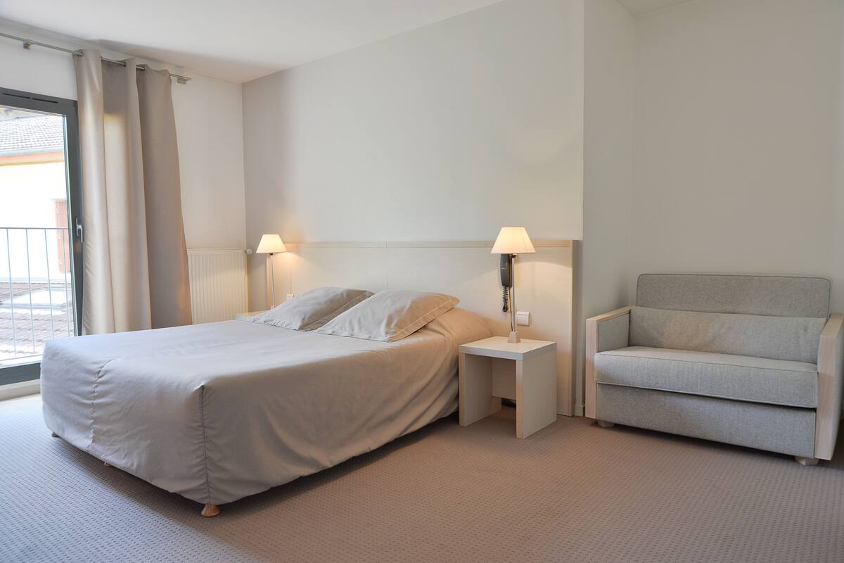 A hotel room with a bed, bedside lamps, a chair, and a view of the outdoors.