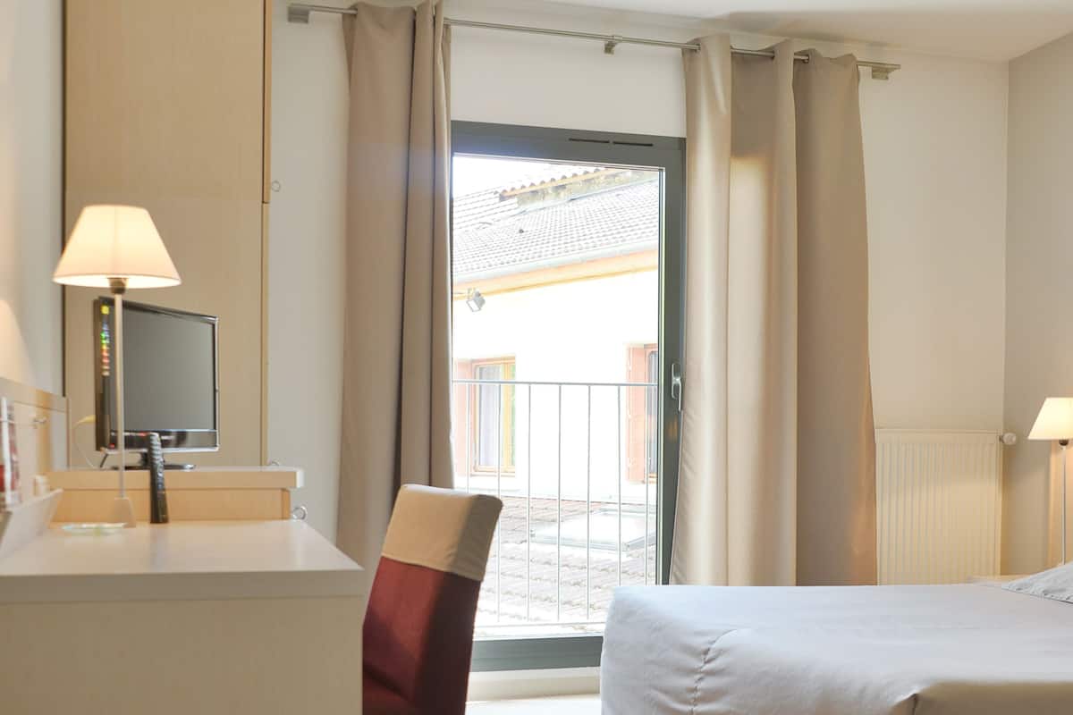 A hotel room with a bed, a desk with a chair, a TV, and a view of the outside.