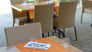 An outdoor dining area with wicker chairs and tables, each set with a wine glass and cutlery.
