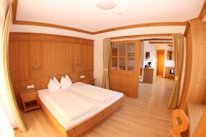 Um quarto espaçoso com uma cama grande, guarda-roupa de madeira e vista para a cozinha.