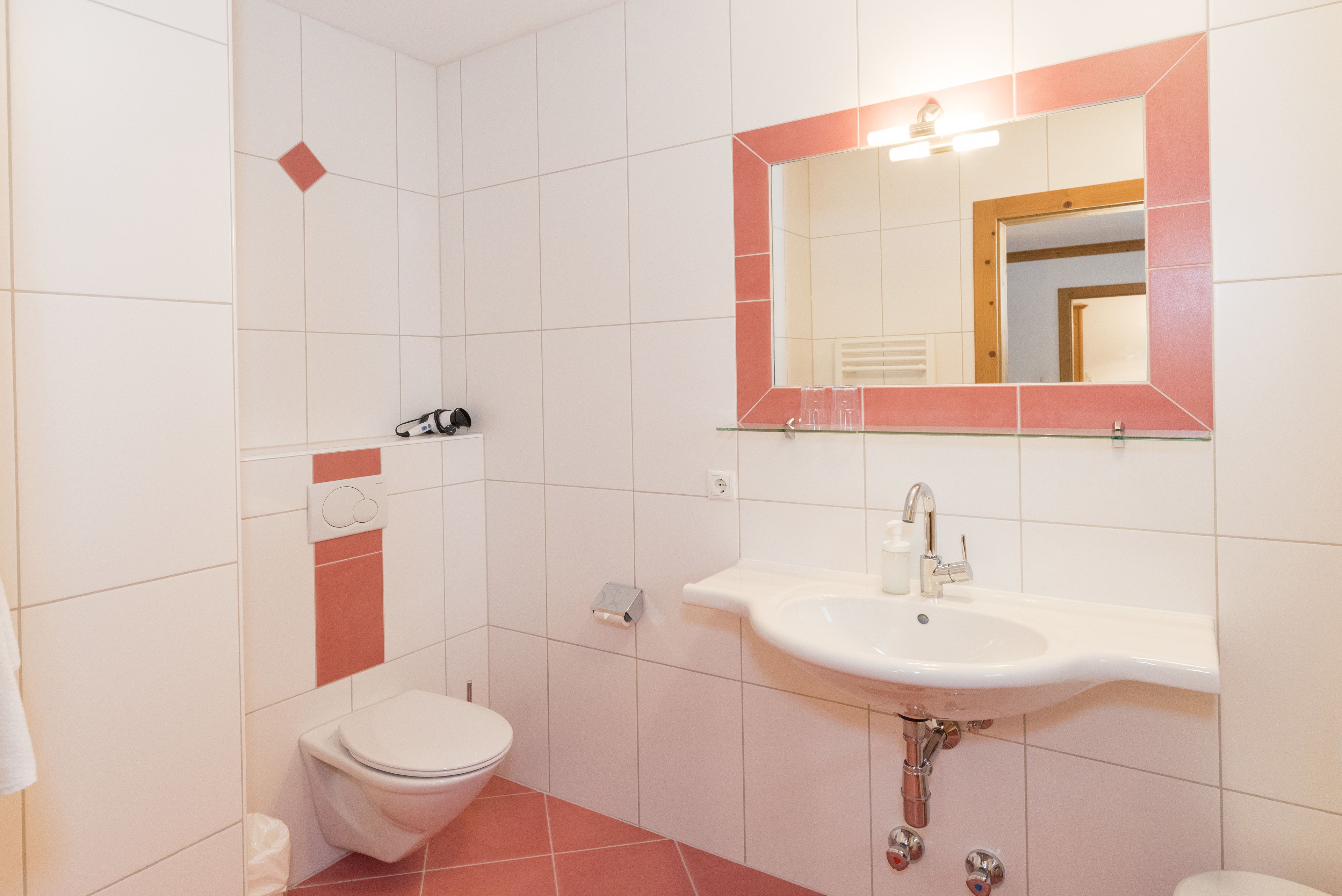 A bathroom with a white toilet, a sink with a mirror above it, and a red-tiled floor.
