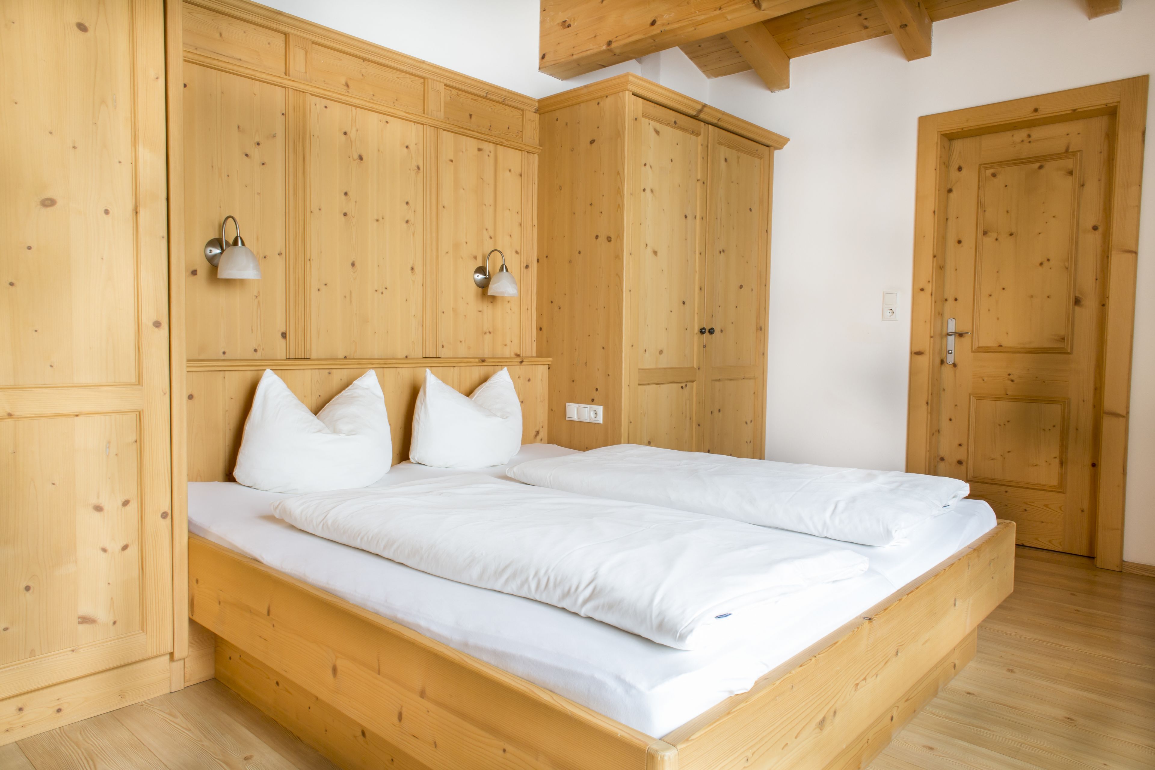 A wooden bed with white bedding in a room with wooden walls and doors.
