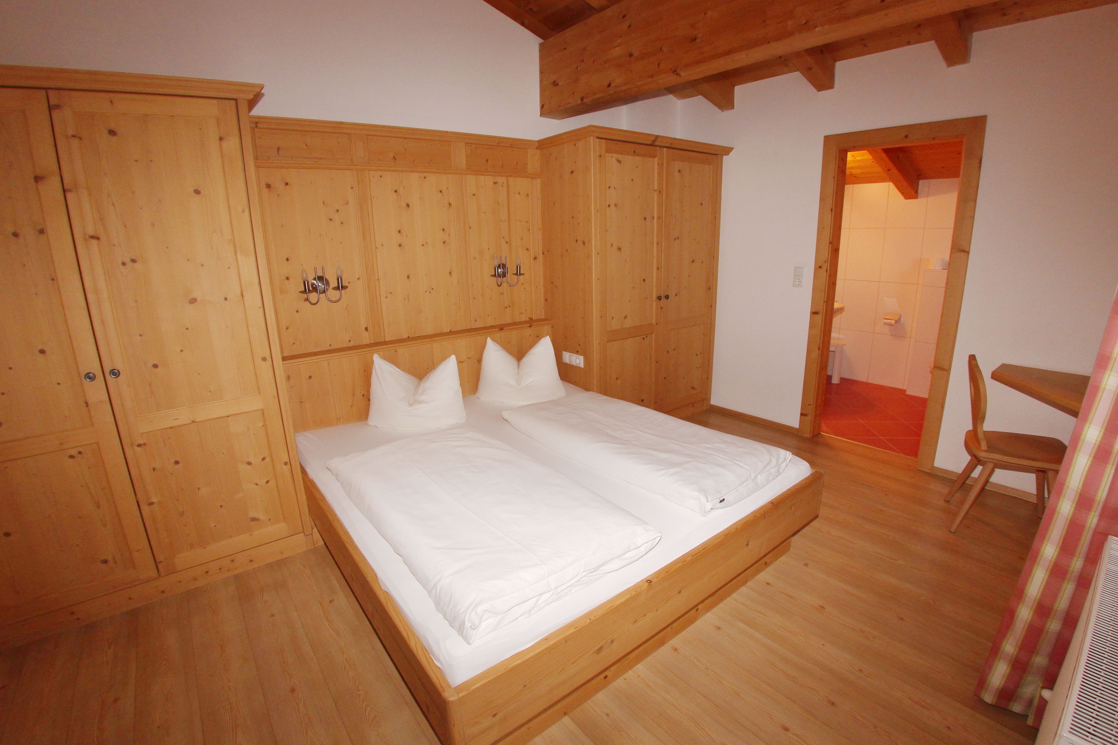 A wooden bedroom with a bed, wardrobe, and a small table.