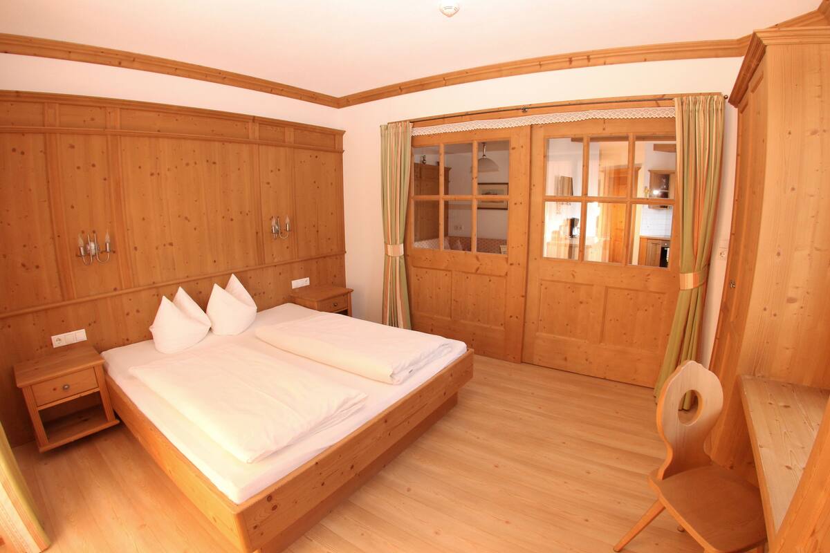 Un dormitorio de madera con una cama grande, una mesita de noche, una silla de madera y un armario.
