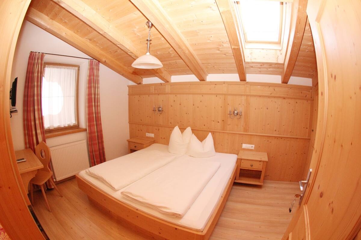 Una habitación de madera con una cama, un escritorio y un ventanal con cortinas.