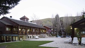 A lodge with a stone patio, outdoor seating, and a view of the surrounding forest. - Rincon de los Andes Resort (San Martín de los Andes)