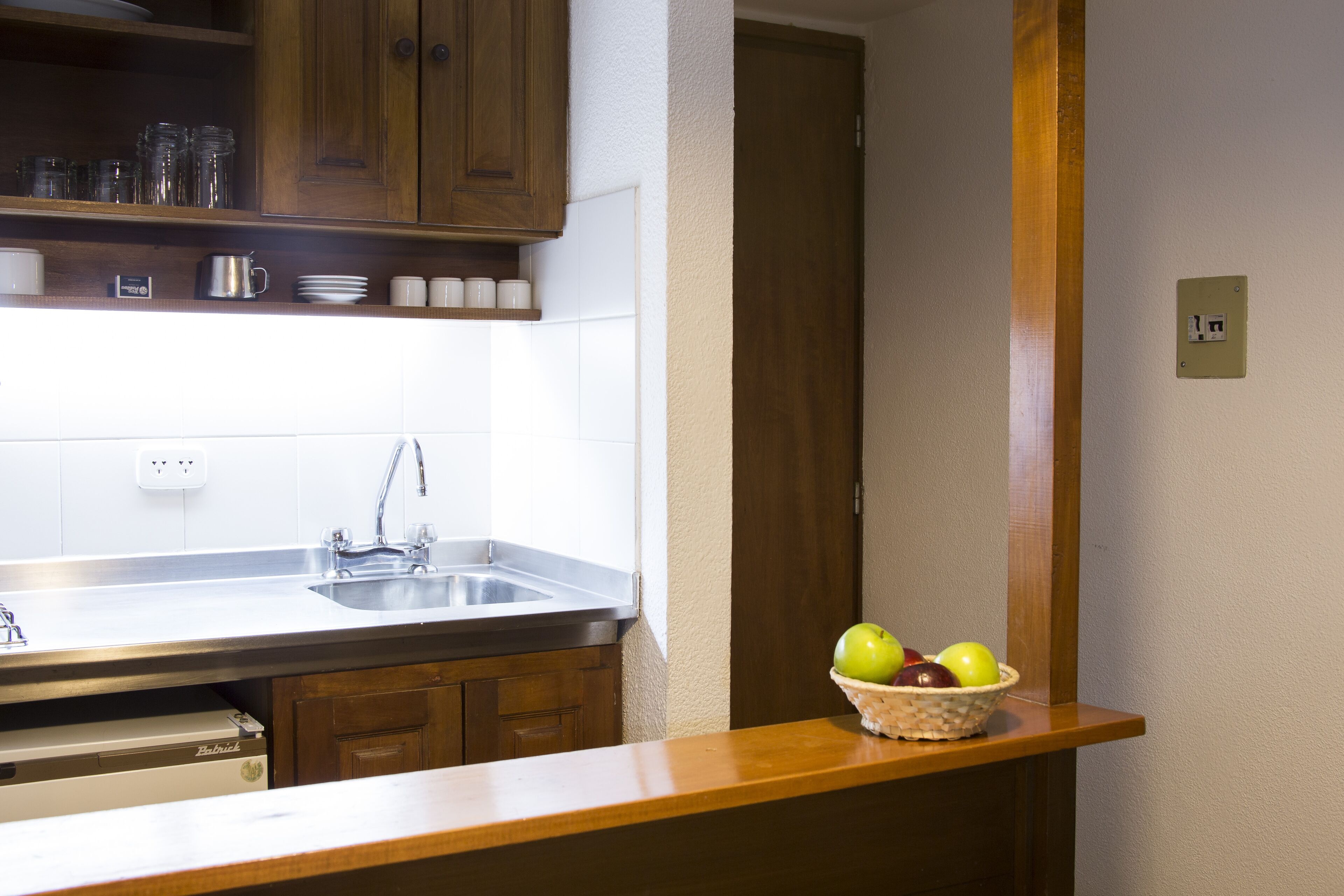 A kitchen with wooden cabinets, a stainless steel sink, and a countertop with a basket of apples.