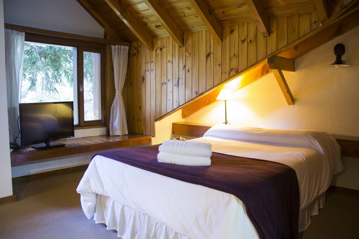 A bedroom with a bed, a TV, and a window with curtains.