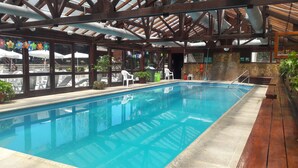 An indoor swimming pool with clear blue water, surrounded by wooden beams and stone walls. - Rincon de los Andes Resort (San Martín de los Andes)