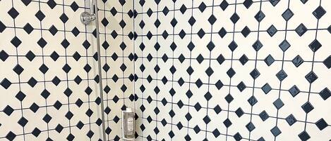 Un baño con una bañera blanca, baldosas con un estampado blanco y negro, y una ducha con cabezal de ducha manual.