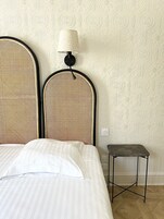 A bed with a striped bedspread, a woven headboard, and a small bedside table with a lamp.