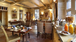 Un grand espace dédié au petit-déjeuner, agrémenté de poutres en bois, de chaises en osier et d’un assortiment de produits pour le petit-déjeuner disposés sur le comptoir.