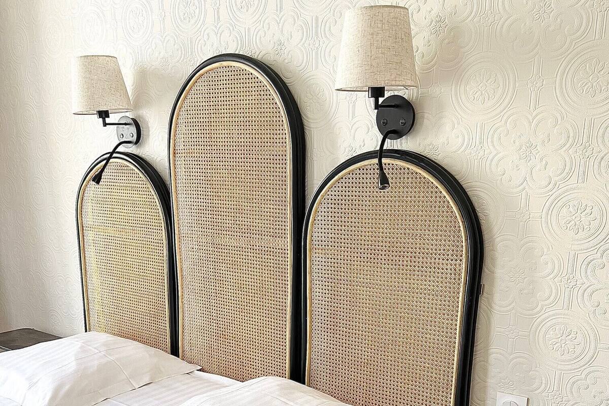 Ein Bett mit weißer Matratze und Kissen, daneben zwei Wandlampen mit beigen Lampenschirmen, vor einer Wand mit einem dekorativen Prägemuster.