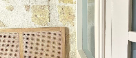 Un dormitorio con pared de piedra, cabecero de madera y ventana con marco blanco.