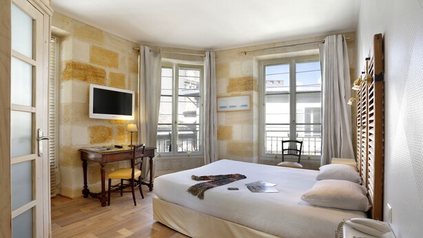 Une chambre d’hôtel avec un grand lit, un bureau avec une chaise, un téléviseur fixé au mur et une fenêtre avec des rideaux.