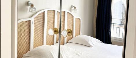 Een slaapkamer met een bed, een spiegel, een raam met gordijnen en een klein tafeltje.