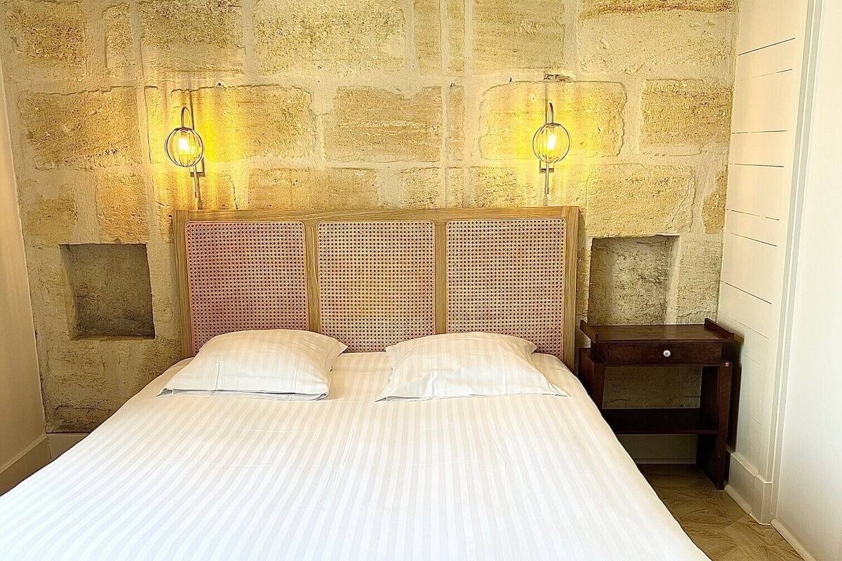 Ein Bett mit Holz-Kopfteil und zwei Wandleuchten vor einer Steinwand.