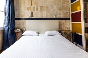 A hotel room with a large bed, a nightstand, a telephone, and a wall with a stone pattern.
