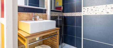 Une salle de bain avec un lavabo blanc, une douche et une étagère avec des serviettes.