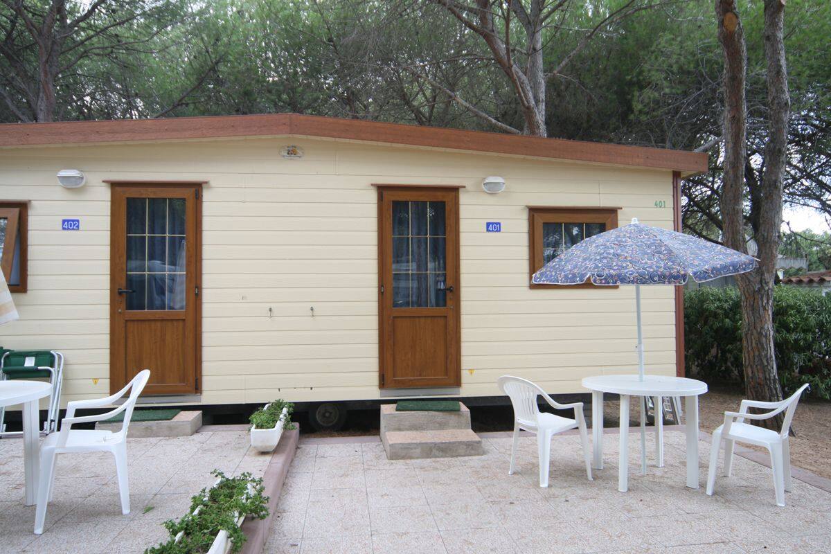 A small, single-story building with two doors and windows, numbered 401 and 402. There are outdoor tables and chairs, and a patterned umbrella.