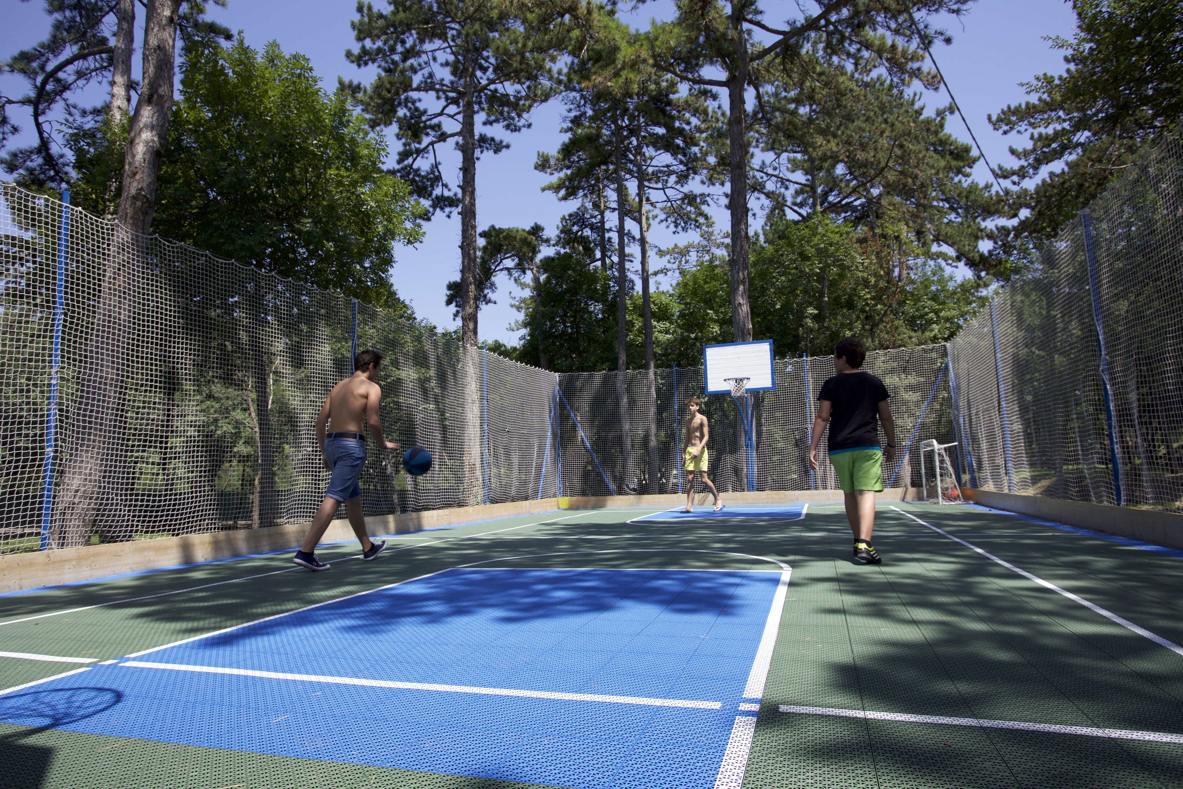An outdoor tennis court with a net, surrounded by trees and a clear sky.