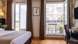 Una habitación de hotel con una cama grande, un escritorio y un balcón con vistas a la ciudad.
