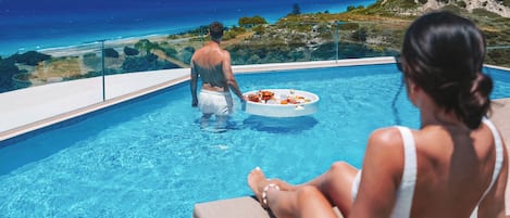 A couple relaxing by a pool with a view of the sea and hills.