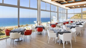 A dining area with tables set for guests, large windows offering a view of the sea, and a wooden ceiling structure. - Atrium Platinum Luxury Resort Hotel & Spa (Rhodes)