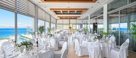 A banquet hall with tables set for a formal event, overlooking a scenic ocean view.
