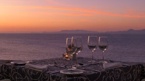 A table set for two with wine glasses and a candle, overlooking a body of water at sunset. - Atrium Platinum Luxury Resort Hotel & Spa (Rhodes)