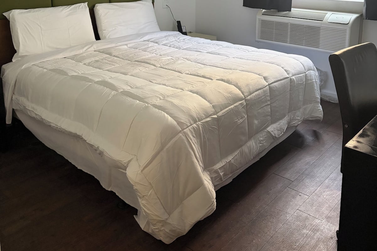 Een hotelkamer met een bed, een groen hoofdeinde, een raam met gordijnen en een wandairconditioner.
