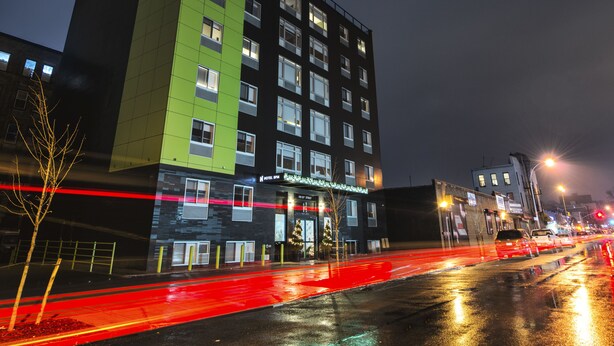 Een hotel met meerdere verdiepingen, een gevel in groen en zwart, veel ramen en een duidelijke ingang.