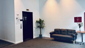 Een receptie met een zwarte liftdeur, een potplant, een leren bank en een kleine tafel met een bloevas.