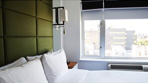 Een hotelkamer met een bed, een raam met uitzicht op gebouwen en een wandlamp.