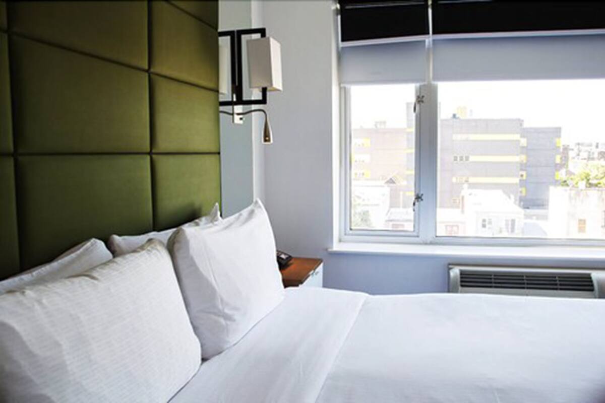 Een hotelkamer met een bed, een raam met uitzicht op gebouwen en een wandlamp.