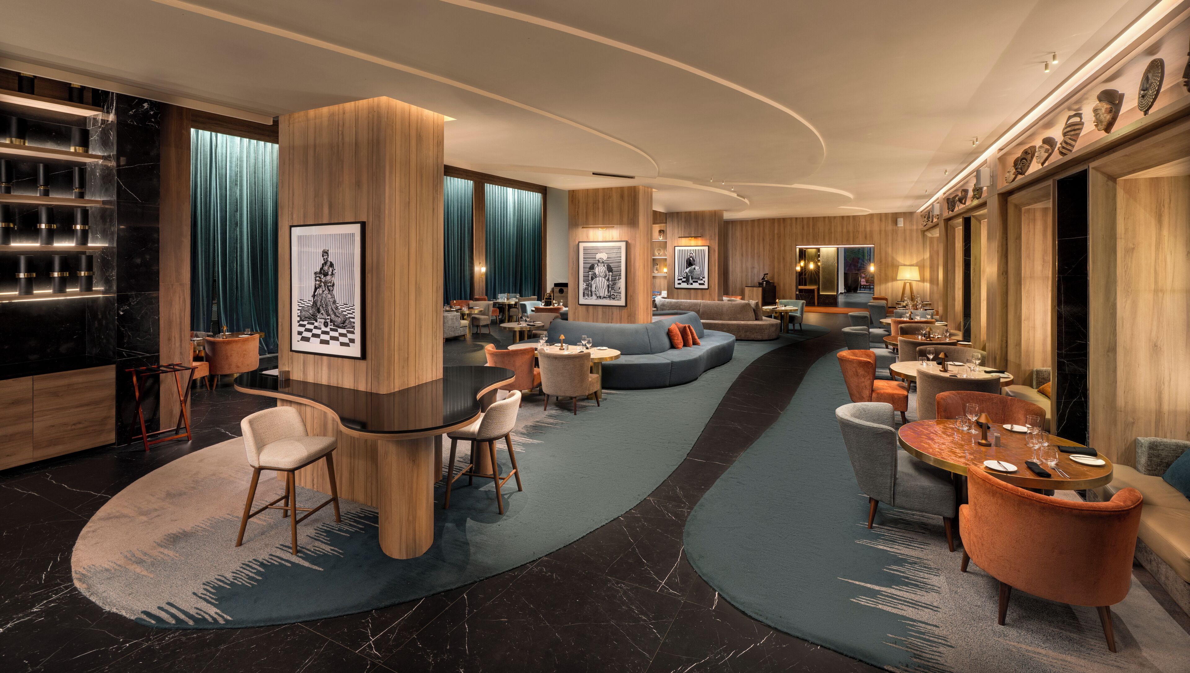 Un moderno hall de hotel con una zona de estar curva, un bar con encimeras de mármol negro y detalles de madera.