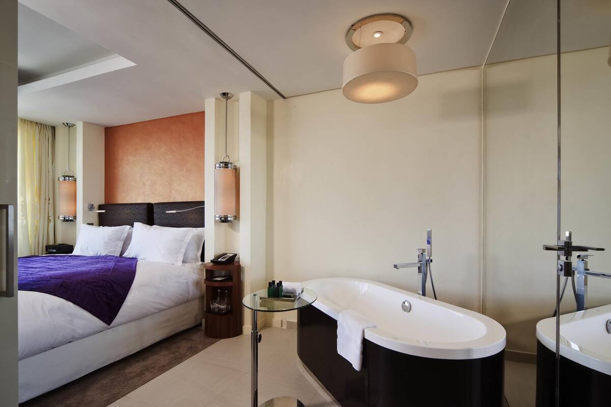 Una habitación de hotel moderna con cama, mesita de noche, lámpara y un espejo grande.