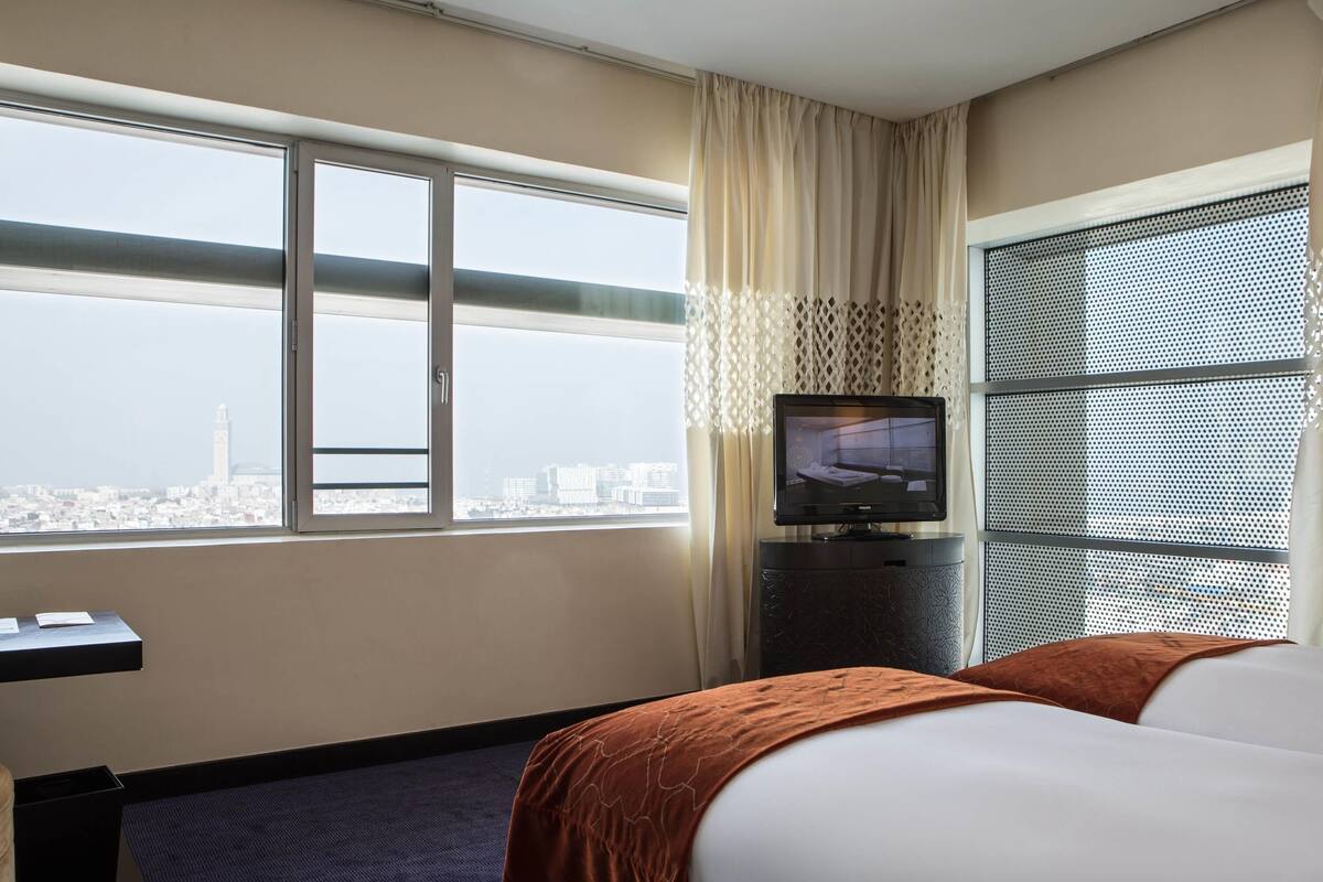 Una habitación de hotel con cama, escritorio, televisión y un ventanal con vistas a la ciudad.