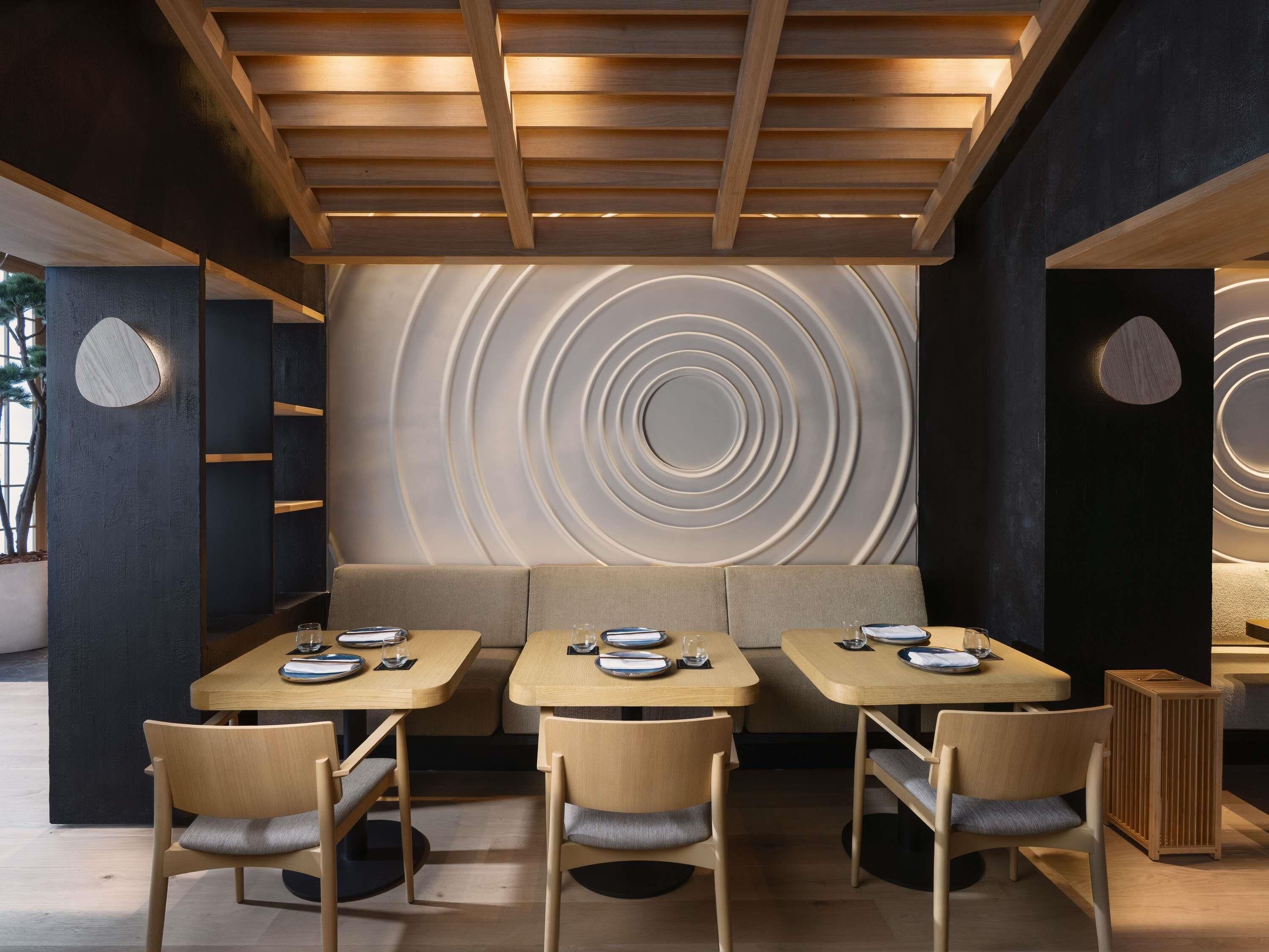 Un área de comedor moderna con mesas y sillas de madera, un diseño de pared circular y un techo con vigas de madera.