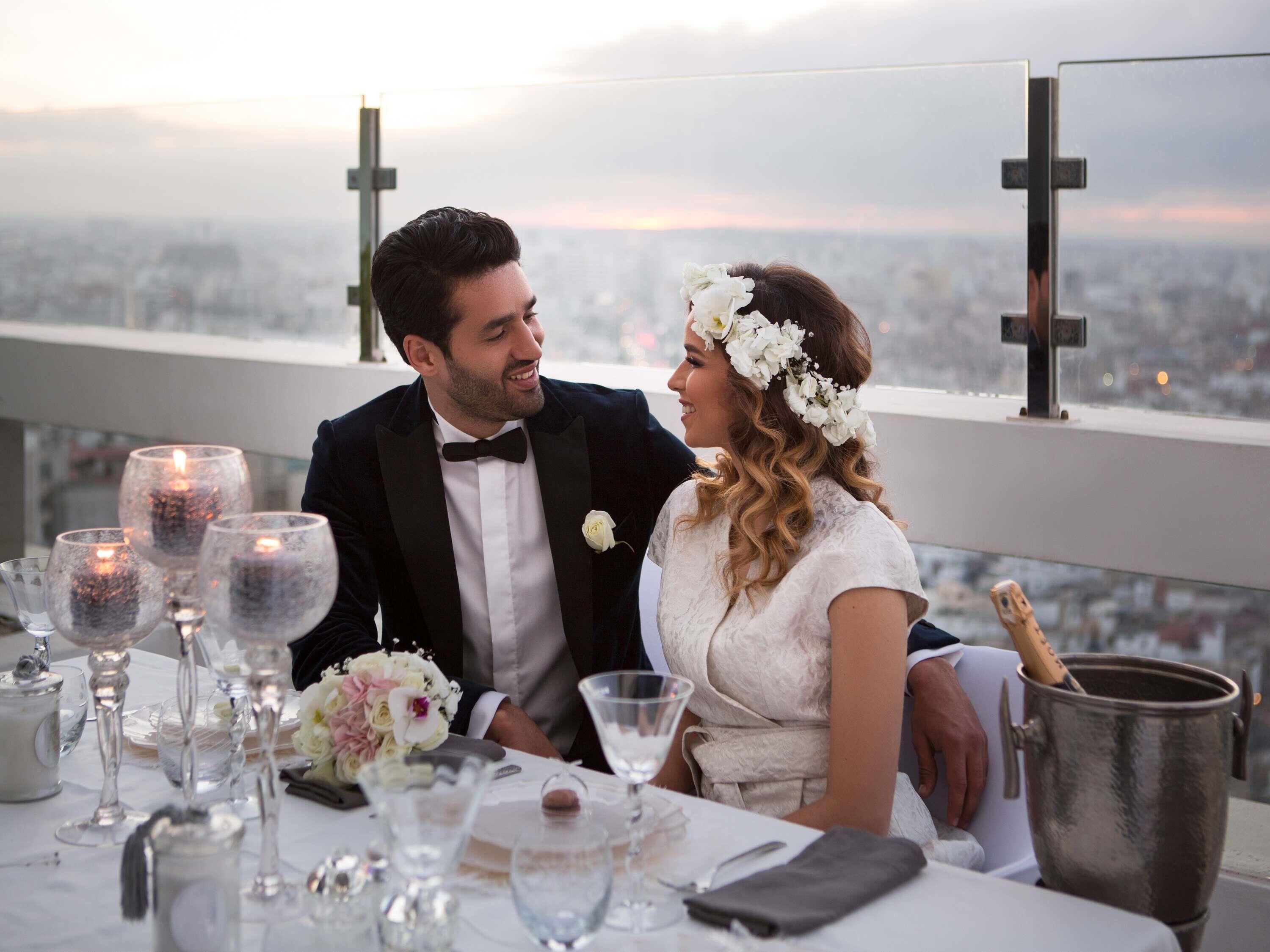Un couple est assis à une table d’où l’on a une vue sur la ville, avec des bougies et un seau à champagne.