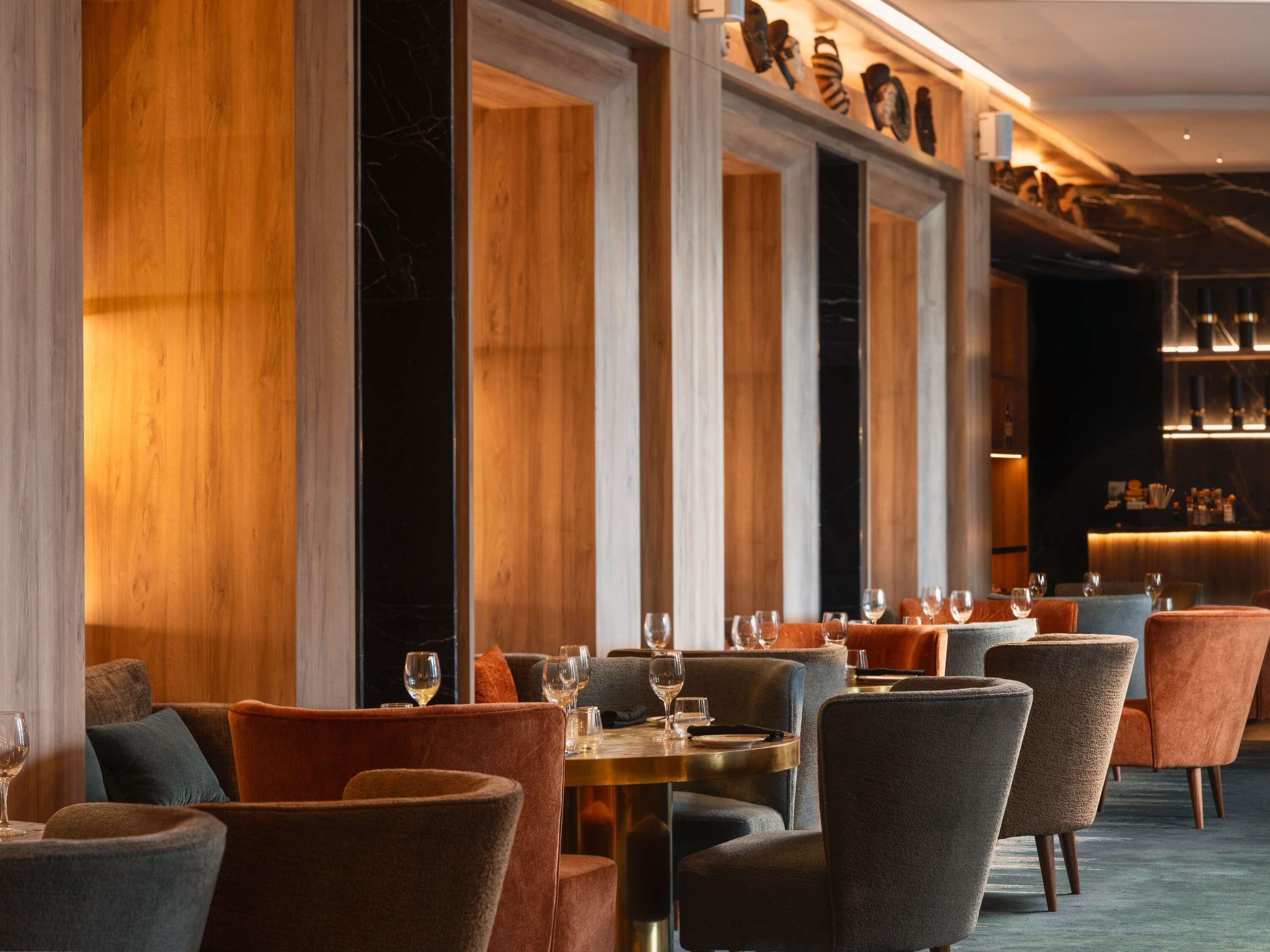 A restaurant with wooden paneling, upholstered chairs, and tables set for dining.