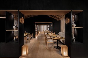 A dimly lit restaurant with wooden tables and chairs, a long counter, and a view of a traditional Japanese room in the background. - Sofitel Casablanca Tour blanche (Casablanca)