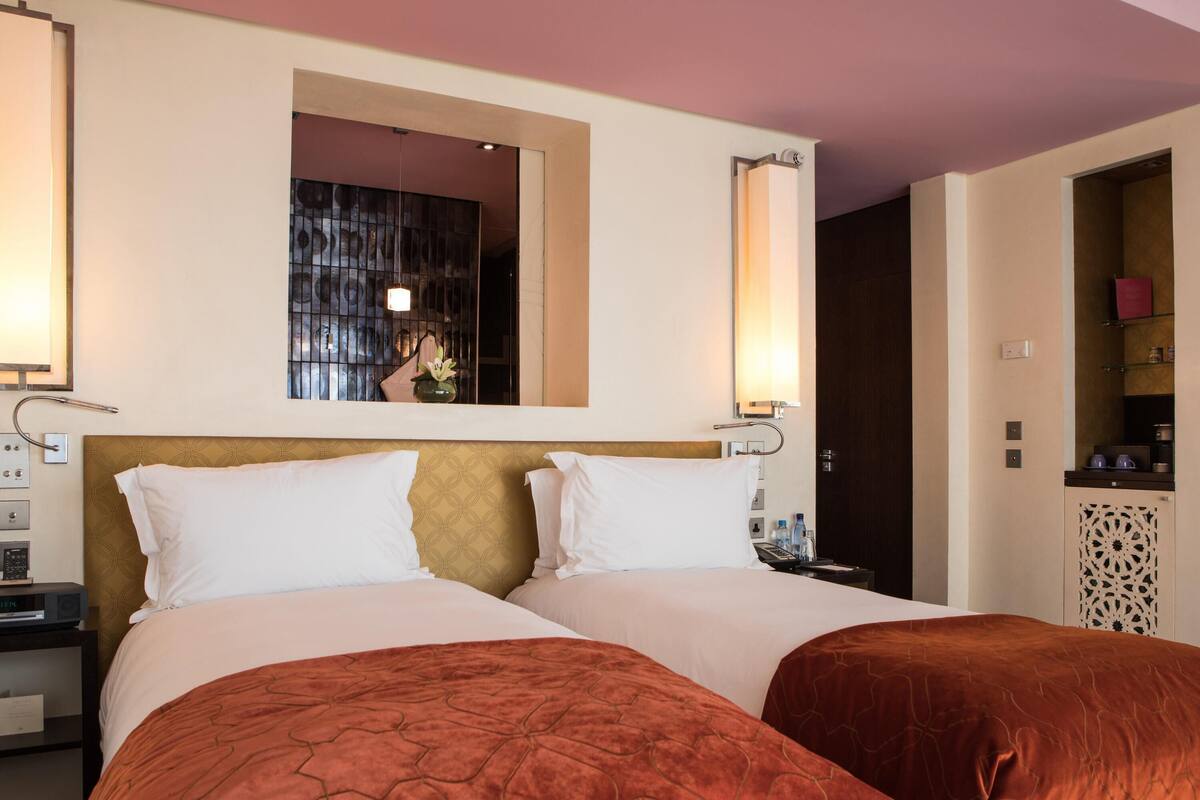 Habitación de hotel con dos camas, un espejo grande, una mesita de noche y un minibar.