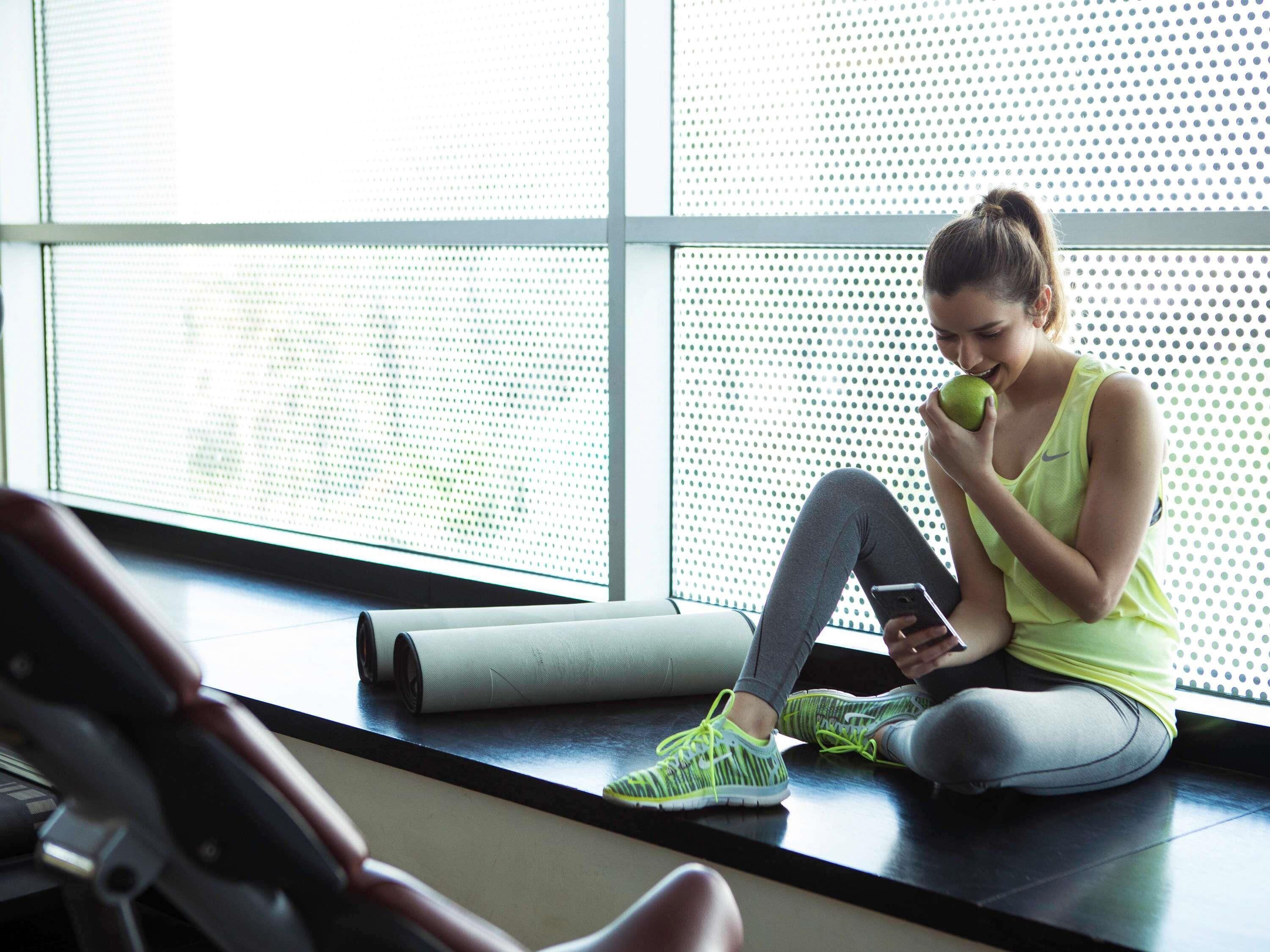 A person sitting on a mat in a room with large windows and exercise equipment.