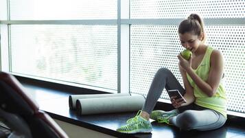 A person sitting on a mat in a room with large windows and exercise equipment.