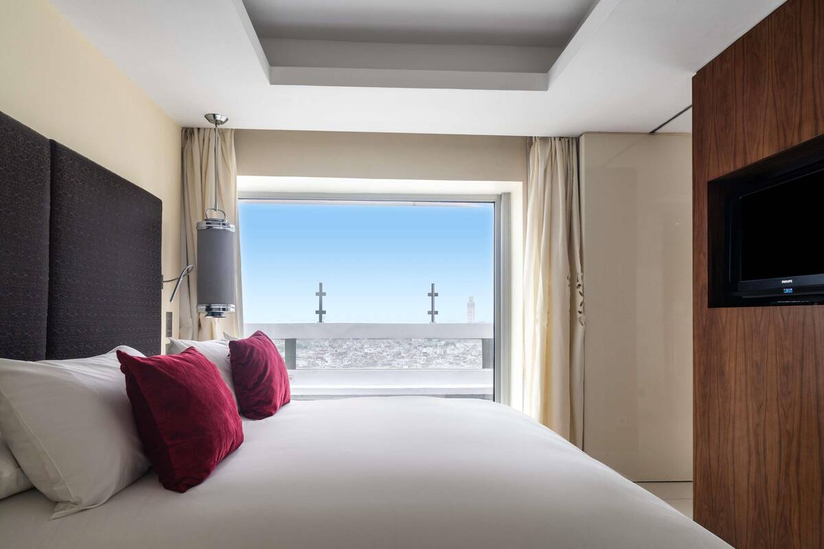Habitación de hotel con una cama grande, televisión, ventana con vista a la ciudad y una lámpara de techo.