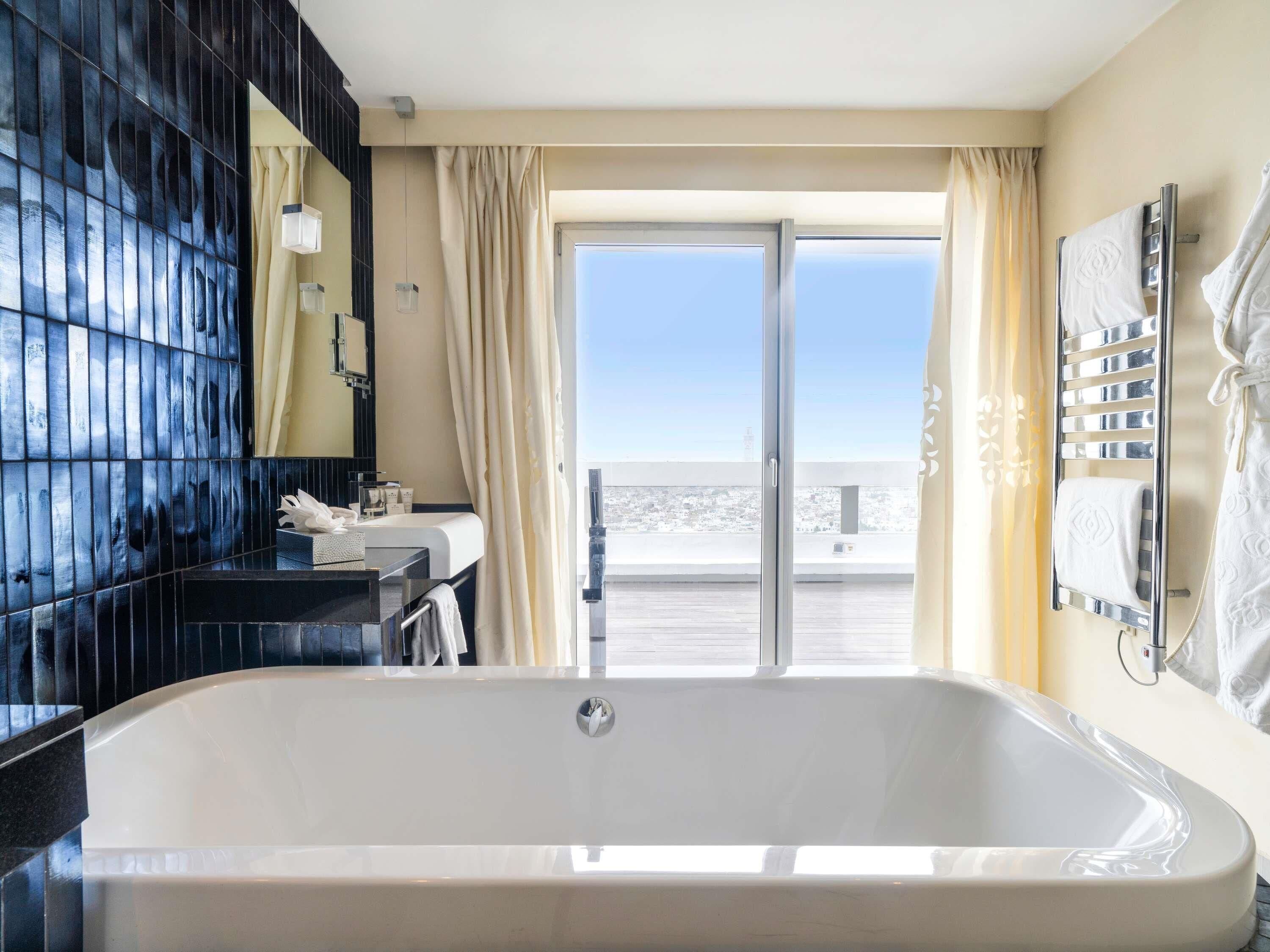 A modern bathroom with a large bathtub, a vanity with a mirror, and a view of the outdoors.