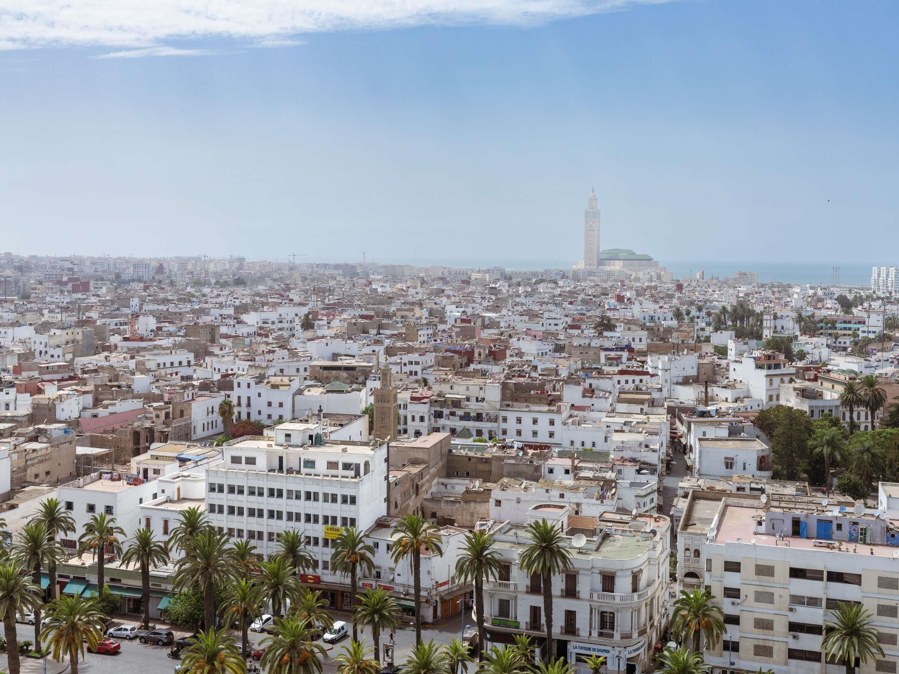 A densely packed urban area with white buildings, palm trees, and a prominent tower in the distance.